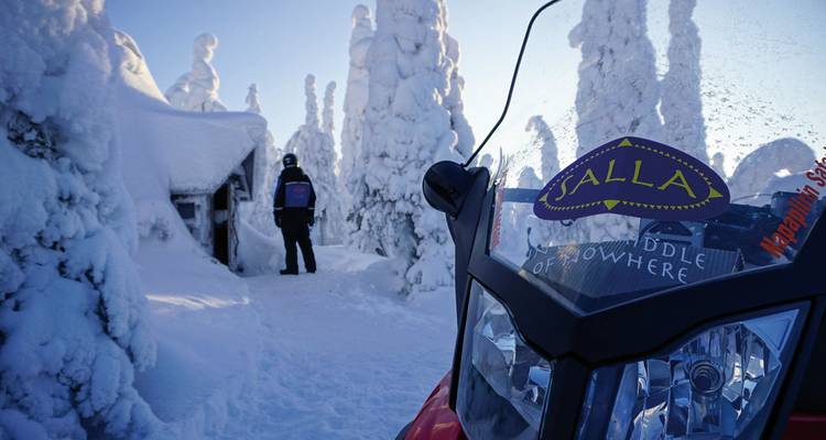 Person mit Schlitten und Schneemobil in schneebedecktem Wald.