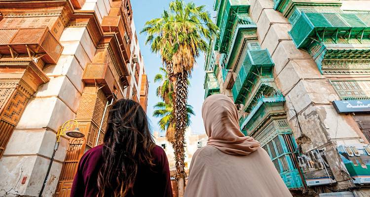 People walking between historic buildings with palm tree