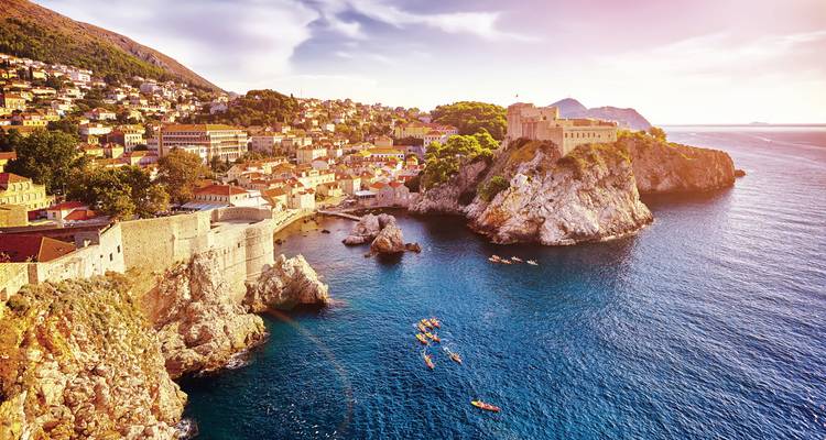 Historische Stadtlandschaft mit Gebäuden auf einer felsigen Küste bei Sonnenuntergang.