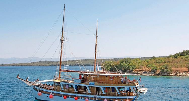 Vintage wooden boat sailing near a rocky coastline on a sunny day.