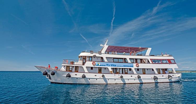 Passagierschiff mit Menschen an Deck unter klarem Himmel auf offener See.