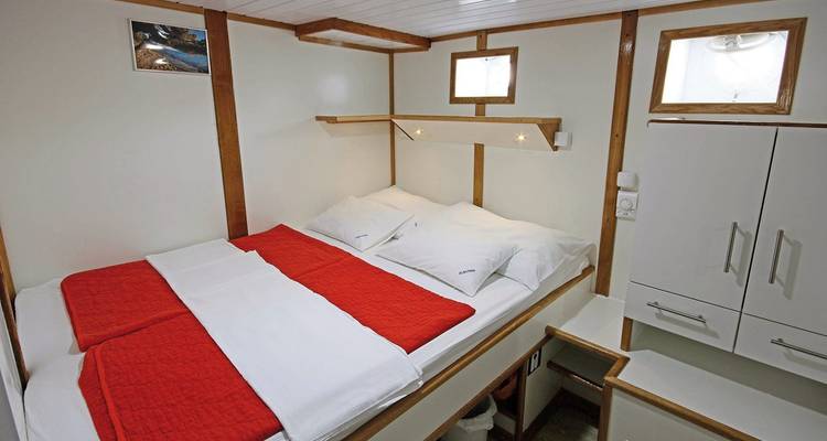 Vista interior de una acogedora cabina de barco con cama doble y ventanas.