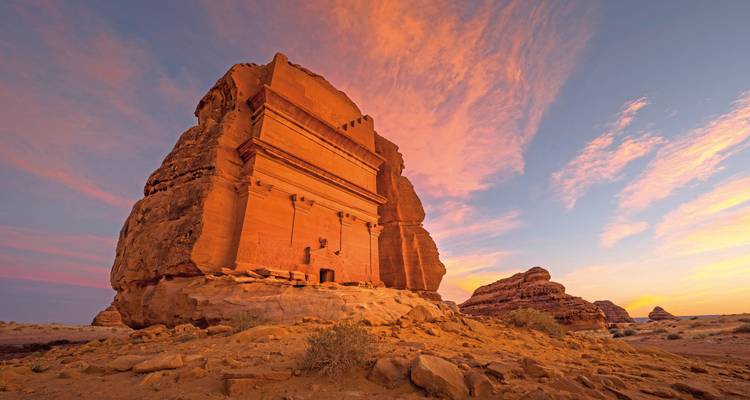 Eine archäologische Stätte mit einem in Fels gehauenen Grab bei Sonnenuntergang.