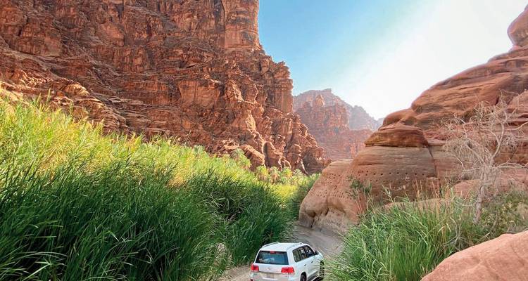 Ein Auto, das durch eine Schlucht mit steilen, roten Felsformationen fährt.