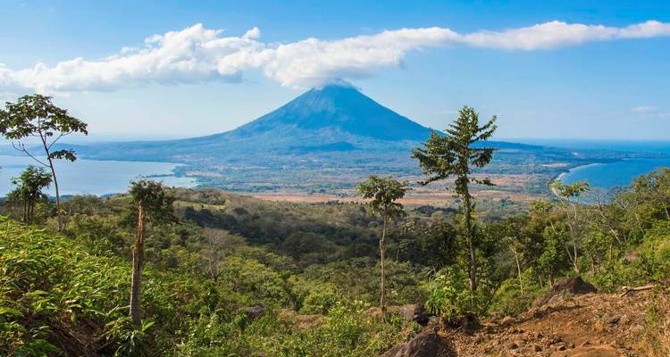 Un volcan dramatique s'élevant au-dessus d'un vaste lac et de terres basses forestières par une journée dégagée