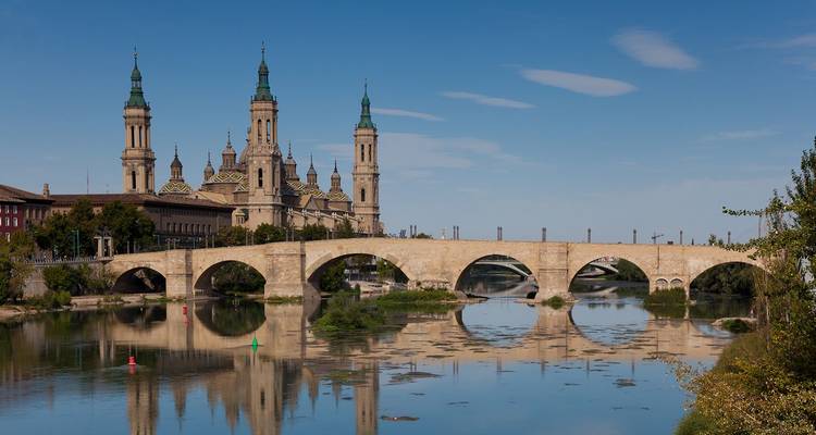 Stenen brug weerspiegeld in de Ebro rivier met de koepels en torens van Zaragoza's Basilica del Pilar.