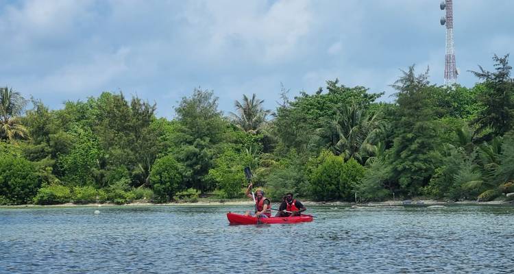 Two kayakers paddle a red canoe across calm turquoise water past lush tropical vegetation.