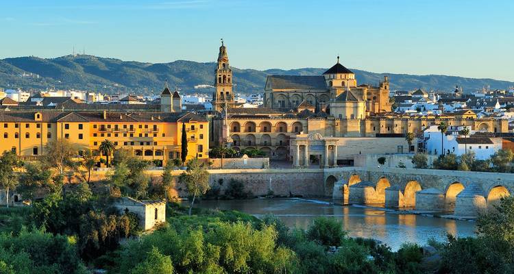 Goldenes Licht beleuchtet die Mezquita-Kathedrale und die römische Brücke von Córdoba, die sich über den Fluss erstreckt, mit entfernten Hügeln im Hintergrund