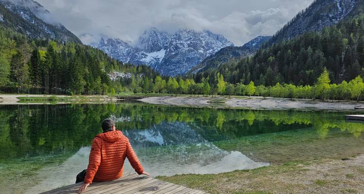 Eine Person, die an einem ruhigen See sitzt, umgeben von Bergen und Bäumen.