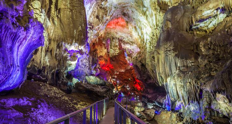 Ein farbenfroh beleuchteter Höhleninnenraum mit einem Geländer, das hindurchführt.