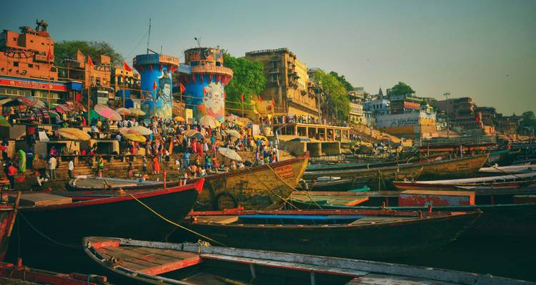 Busy riverbank in Varanasi with boats and vibrant buildings.