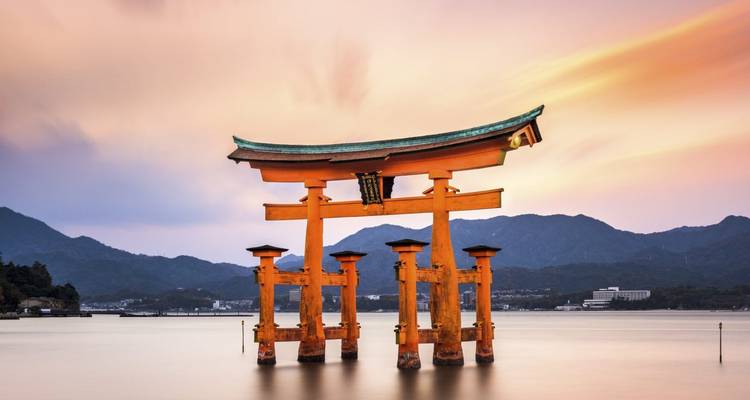 Iconic Japanese torii gate standing in the water at sunset.