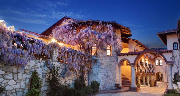 Encantadora posada de piedra cubierta de glicina púrpura bajo el cielo del atardecer con arcos en el patio.