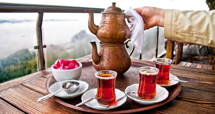 Set de té turco tradicional con tres vasos y tetera de cobre en una bandeja con vistas al agua.