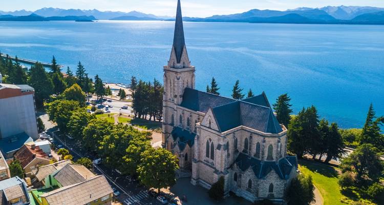 Iglesia de estilo gótico junto a un lago con árboles y montañas.