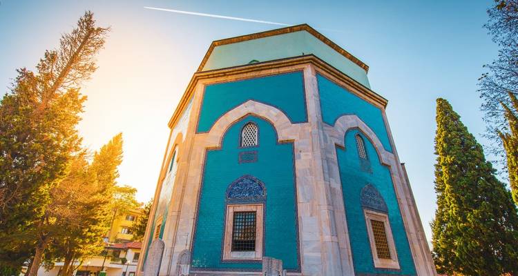 La Tumba Verde octogonal de Bursa cubierta de azulejos turquesa vívidos enmarcada por altos cipreses al atardecer.