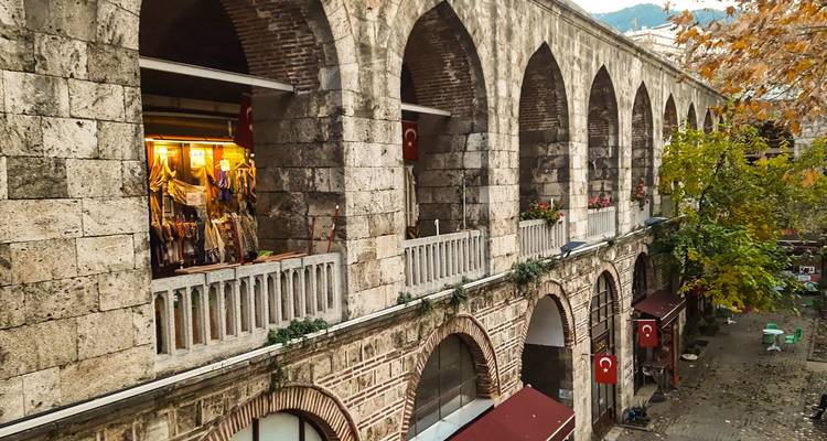 Arcadas de piedra del bazar histórico de Bursa con banderas turcas colgantes y textiles coloridos.
