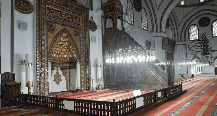 Interior de la mezquita Ulu Cami con mihrab ornamentado y alfombras con patrones iluminadas por una lámpara de araña moderna.