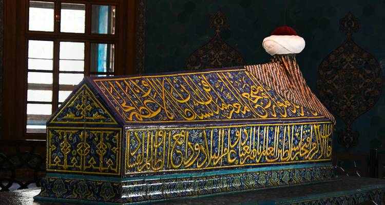 Tumba islámica de azulejos coloridos coronada con un turbante dentro del mausoleo de Bursa.