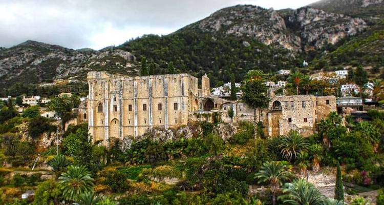 Stone Gothic-style Bellapais Abbey nestled on a green hillside beneath rocky mountains.