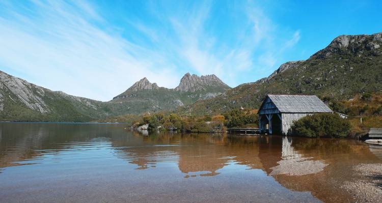 A boathouse next to a serene lake surrounded by peaks.