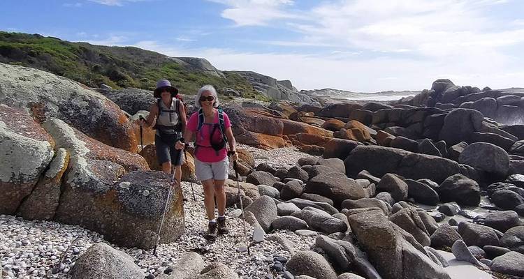 Deux randonneurs avec des bâtons naviguent le long d'une côte rocheuse sous un ciel dégagé