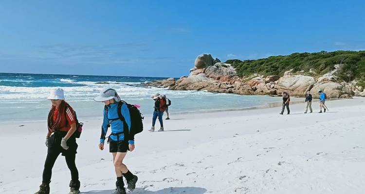 Petit groupe de randonneurs marchant le long d'une large plage blanche à côté d'un ressac turquoise