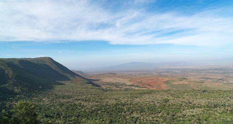 Weite Aussicht auf eine grüne und felsige Landschaft mit Bergen in der Ferne unter einem blauen Himmel.