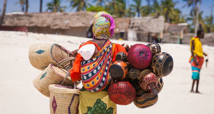 Person carrying traditional baskets on a beach.