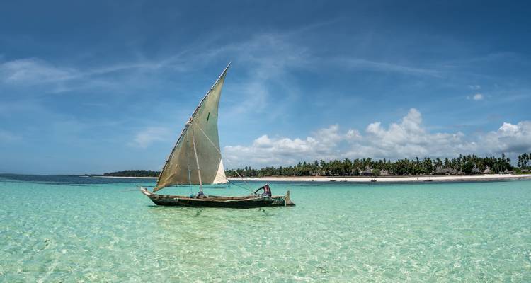 Traditional dhow boat sailing in clear blue waters.