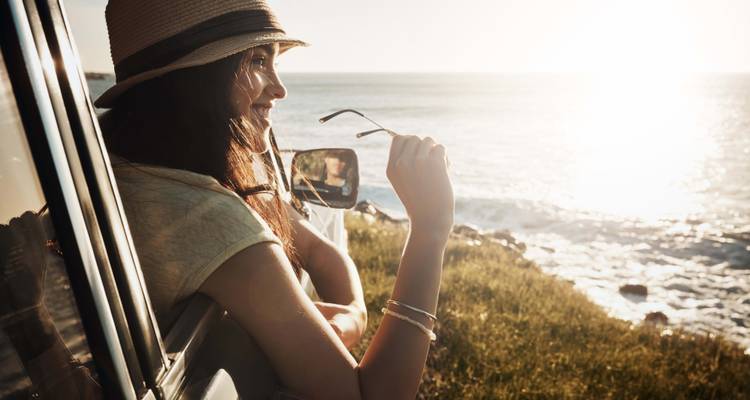Frau in einem Auto, die auf das Meer blickt mit sonnenbeschienener Landschaft.