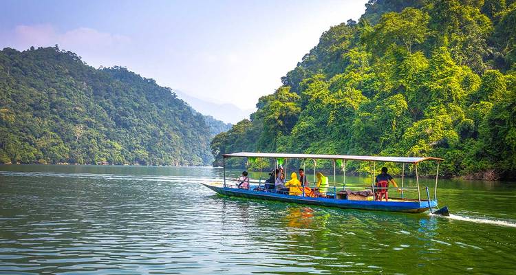 Bateau sur une rivière entouré d'arbres verts et de collines.