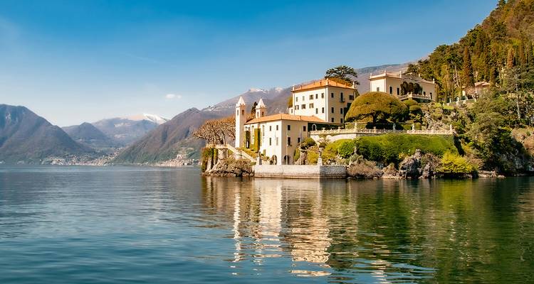 An elegant villa sits on a wooded promontory reflected in the calm waters of Lake Como.