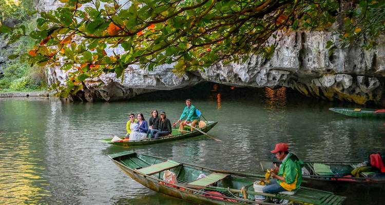 De petits canots à rames avec des touristes pagaient en direction de l'entrée d'une grotte calcaire sur une rivière verte calme.