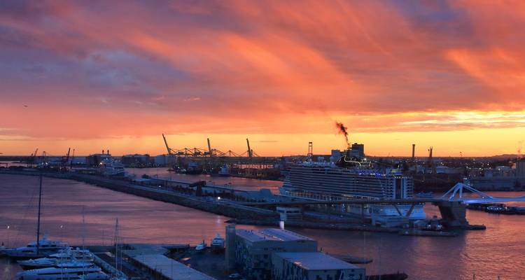 Cruise ship docked at a harbor under a fiery sunset.