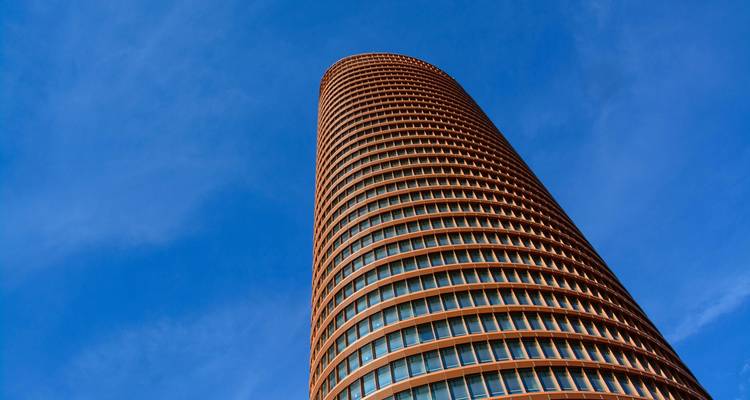 Modern cylindrical skyscraper against a blue sky.