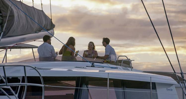 People enjoying drinks on yacht deck with sunset view.