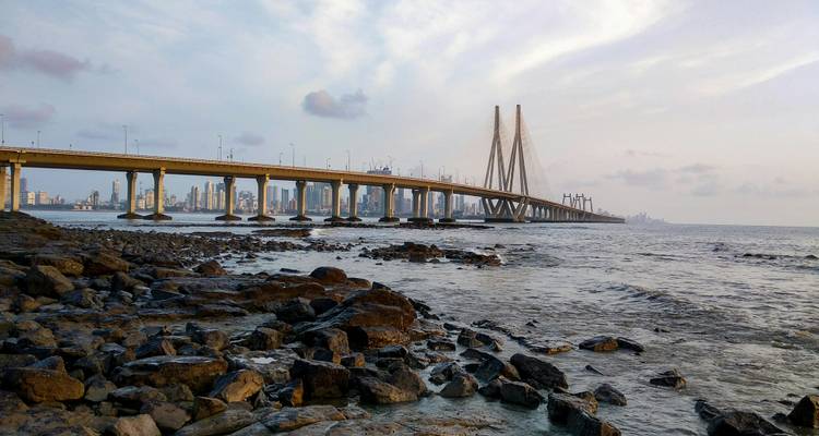 Puente Bandra-Worli Sea Link extendiéndose sobre la costa rocosa con el horizonte de la ciudad de fondo.