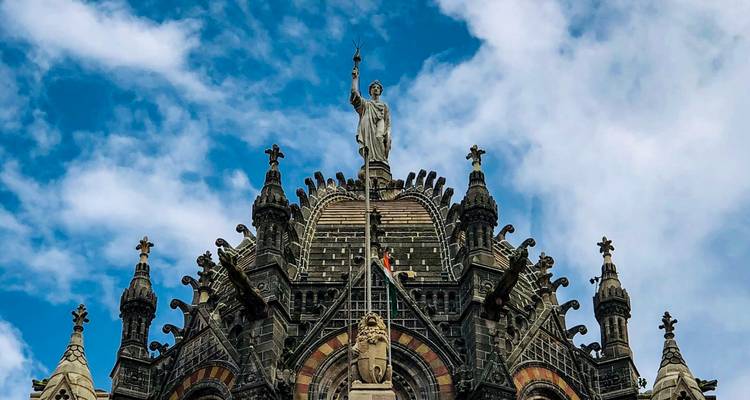Estatua de pináculo ornado en la parte superior de un edificio histórico contra un cielo nublado y dramático.