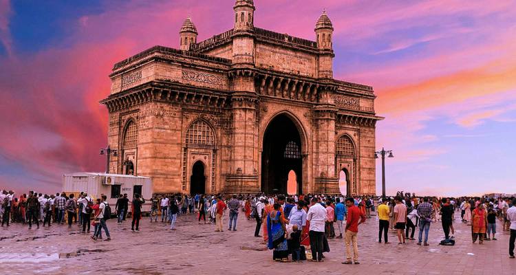 Plaza Gateway of India llena de visitantes bajo un cielo de atardecer rosa vívido.