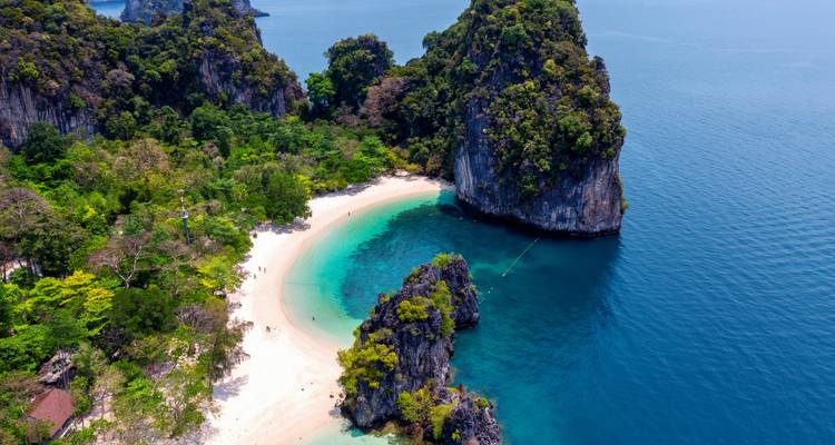 An aerial view of a secluded bay with green cliffs and clear blue waters.