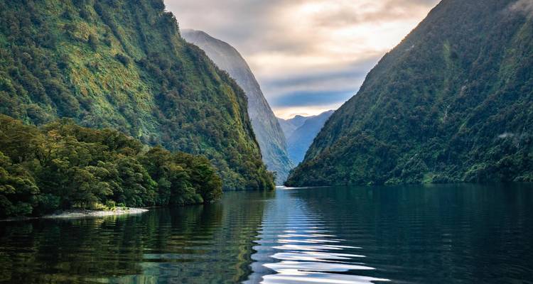 Still fjord waters reflect steep green walls leading into distant misty mountains.