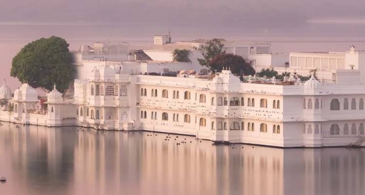Un palais de marbre blanc qui semble flotter sur le lac Pichola tranquille dans la lumière douce et pastel de l'aube voilée.