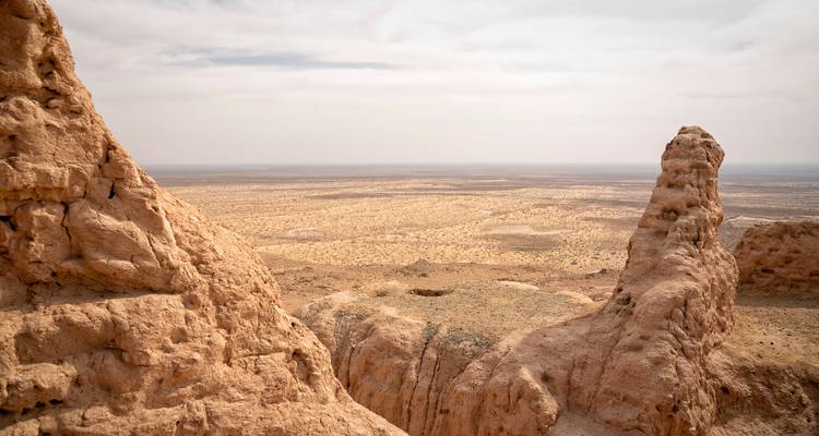 Eroded desert cliffs overlook an endless arid plain beneath a hazy sky in Central Asia.
