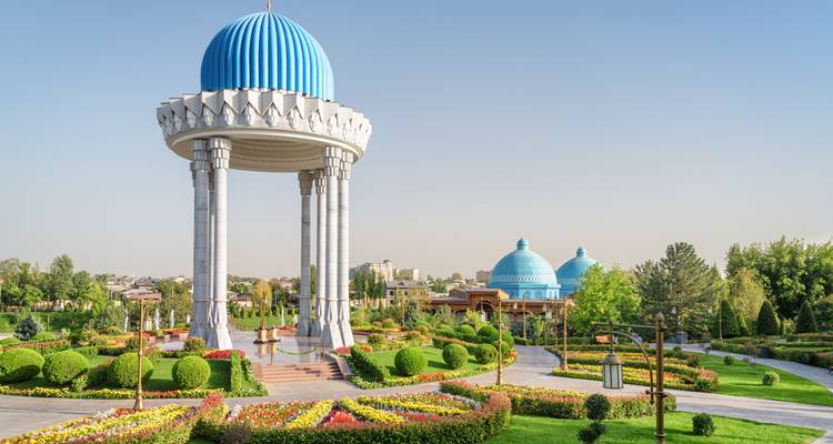 Elegant white pavilion with a bright blue domed roof stands amid manicured flower gardens in Tashkent.