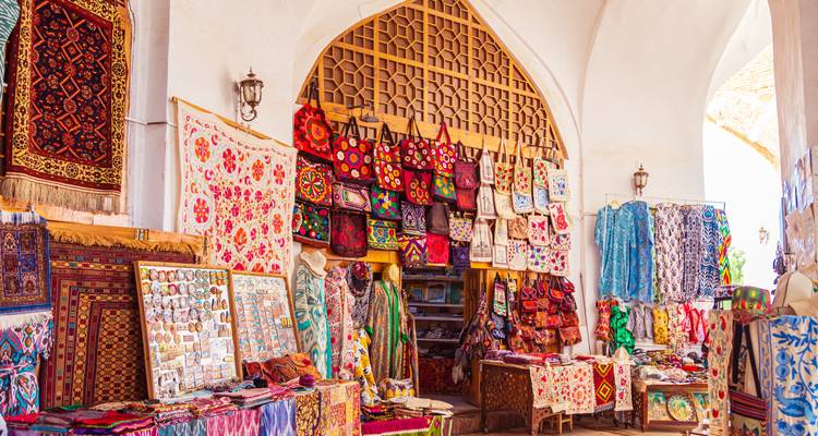 Colorful carpets, bags and textiles fill a vaulted bazaar stall in Uzbekistan.