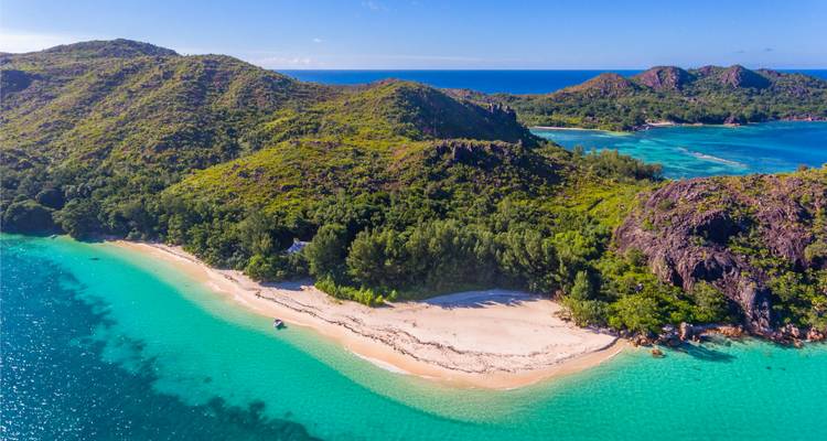 Vue panoramique d'une plage isolée avec des collines verdoyantes en arrière-plan.