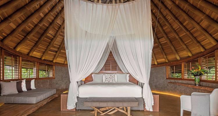 Canopy bed under a wooden ceiling with seating area.