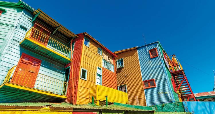 Reihe von leuchtend bemalten Wellblechhäusern im Stadtteil La Boca vor klarem blauem Himmel