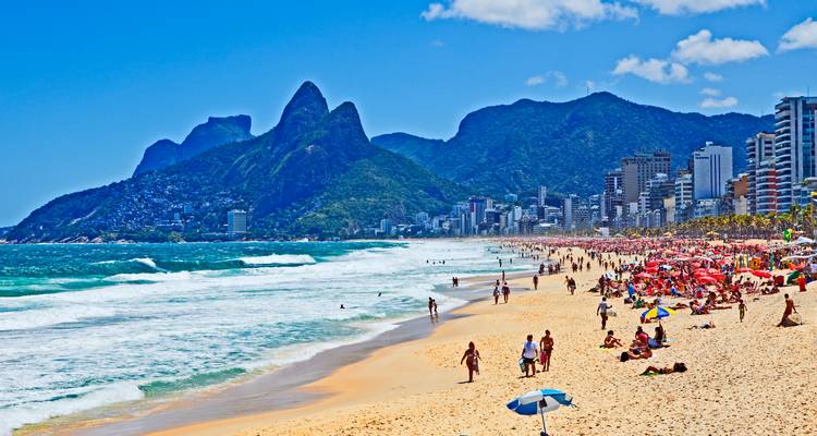 Playa de Ipanema abarrotada en Río de Janeiro con montañas.